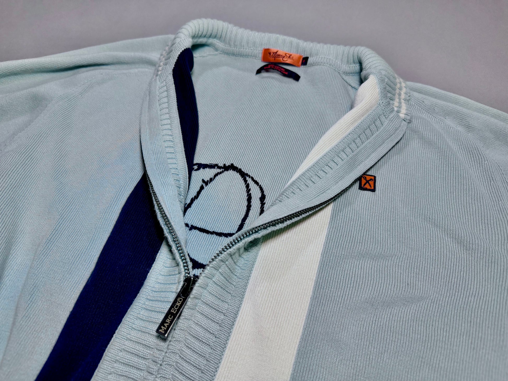 Close-up of the Marc Ecko cardigan front showing zip collar, stripe detail, and embroidered logo.