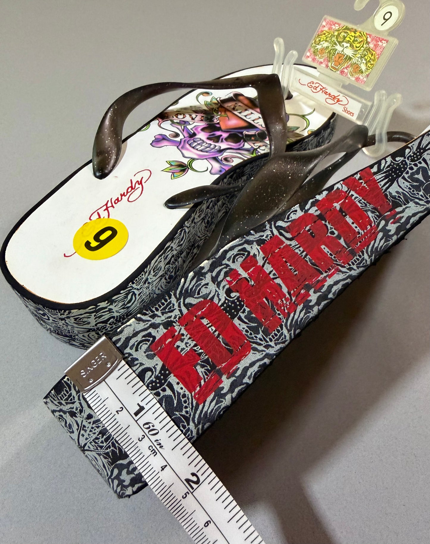 Side view of Ed Hardy platform flip-flops showing black-and-gray tattoo-print wedges, distressed red logo, and approximately 1.5-inch platform height.