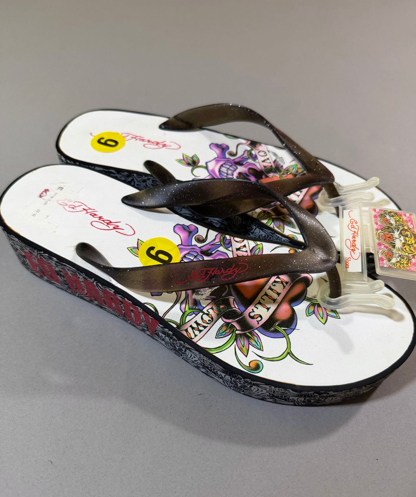 Vintage Ed Hardy women’s platform flip-flops with glitter straps, colorful skull-and-rose footbeds, and black tattoo-print wedge soles, size 9.