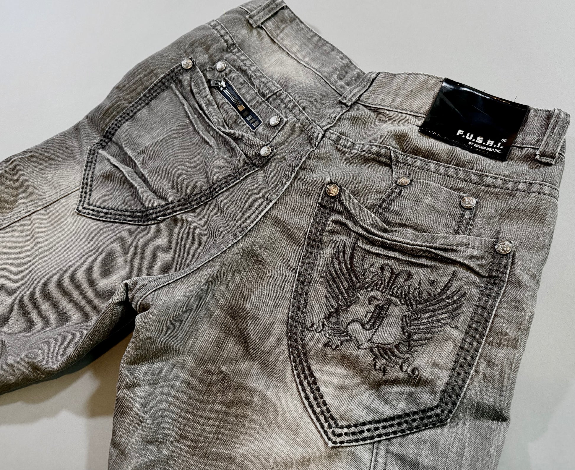 Close-up of embroidered back pocket, zipper detail, logo hardware, and black F.U.S.A.I. patch.