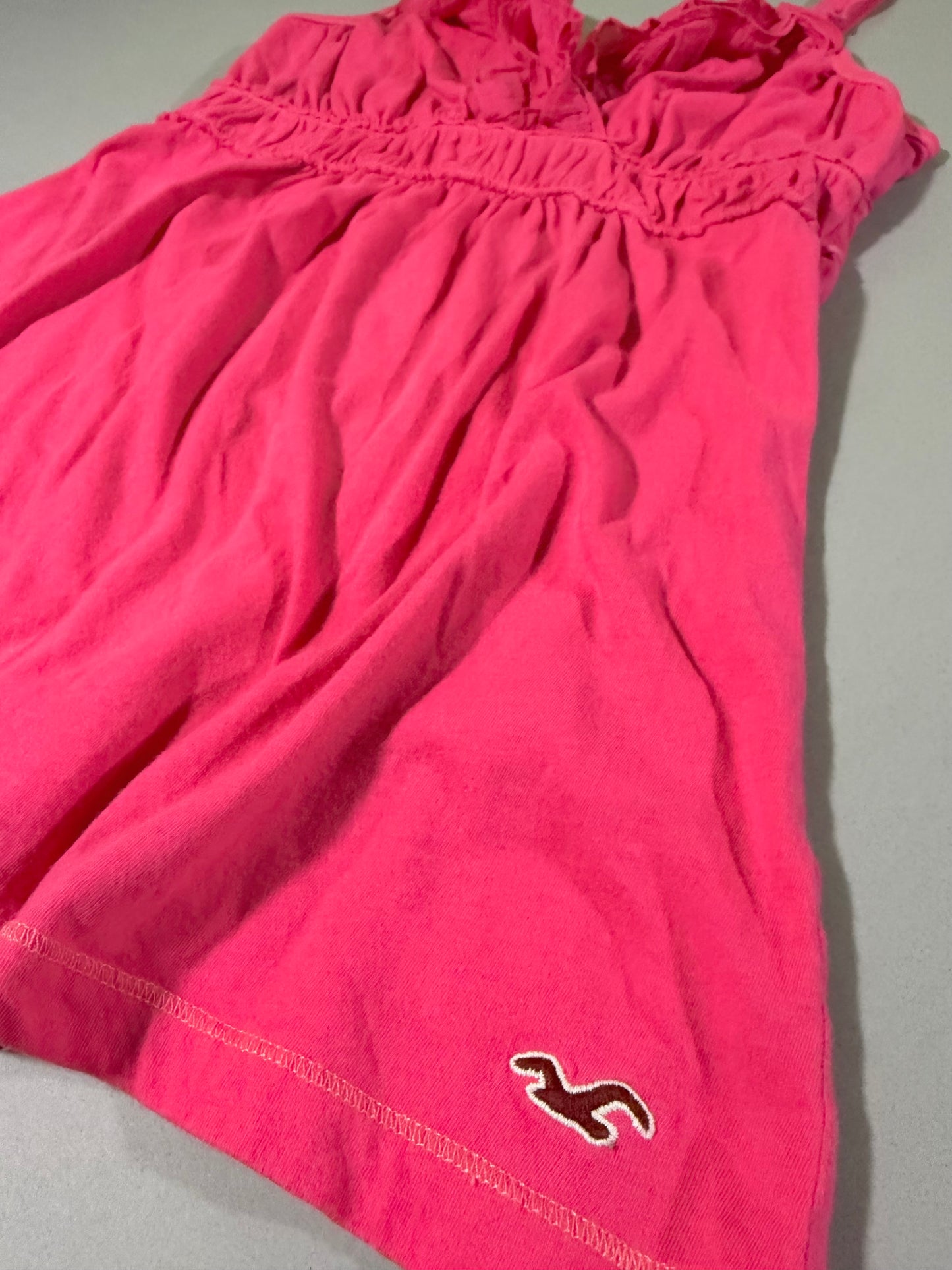     Close-up of the coral pink Hollister babydoll tank top showing the gathered fabric, contrast stitching and embroidered seagull hem logo.