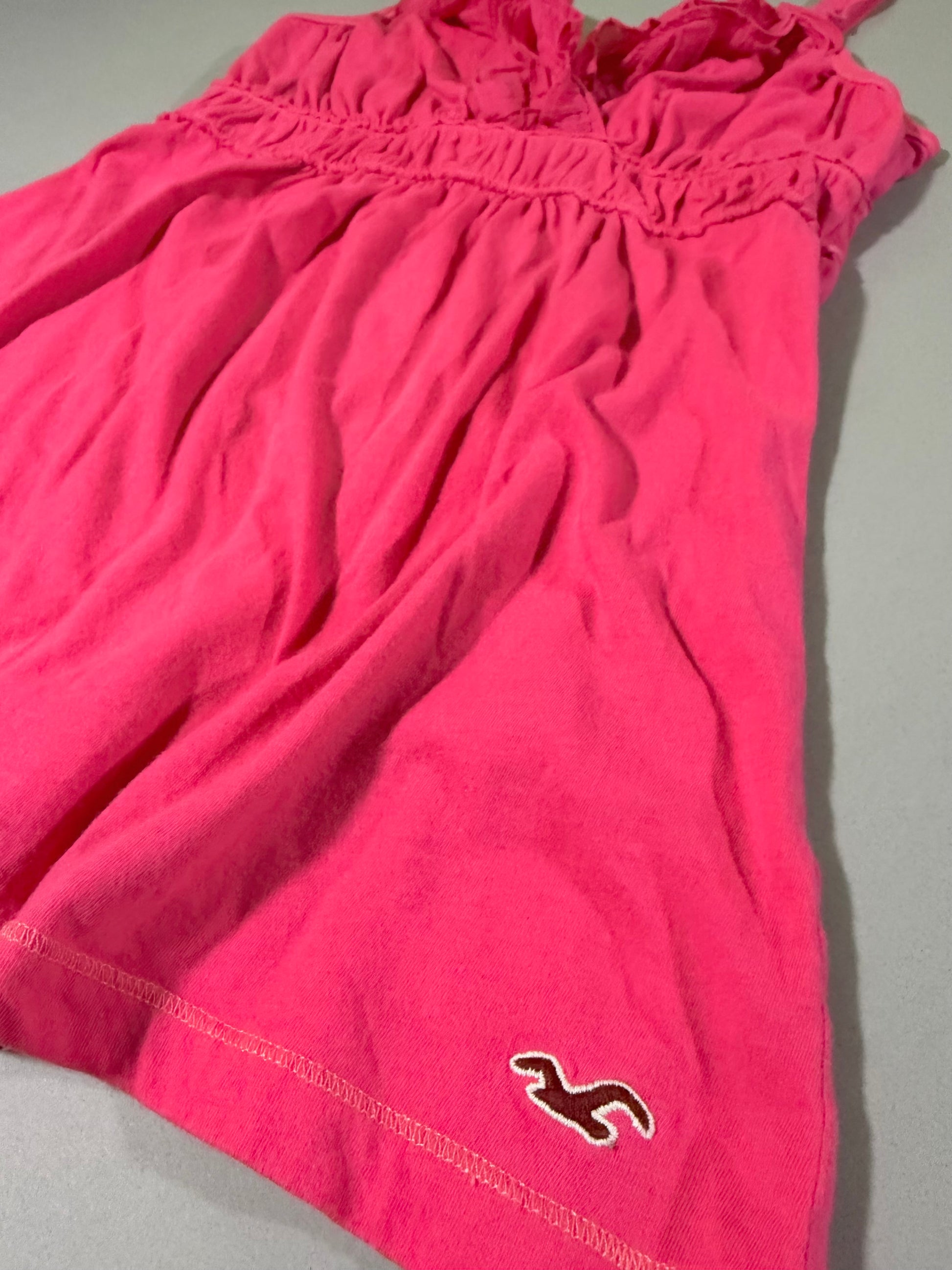     Close-up of the coral pink Hollister babydoll tank top showing the gathered fabric, contrast stitching and embroidered seagull hem logo.