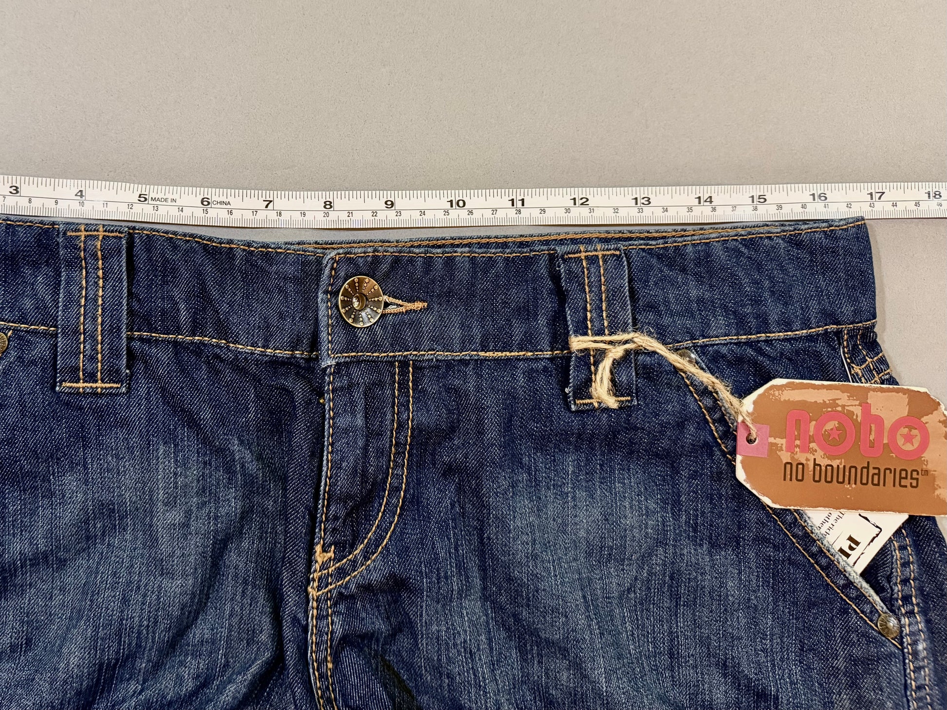Close-up of waistband, button closure, belt loops, and original Nobo hang tag.