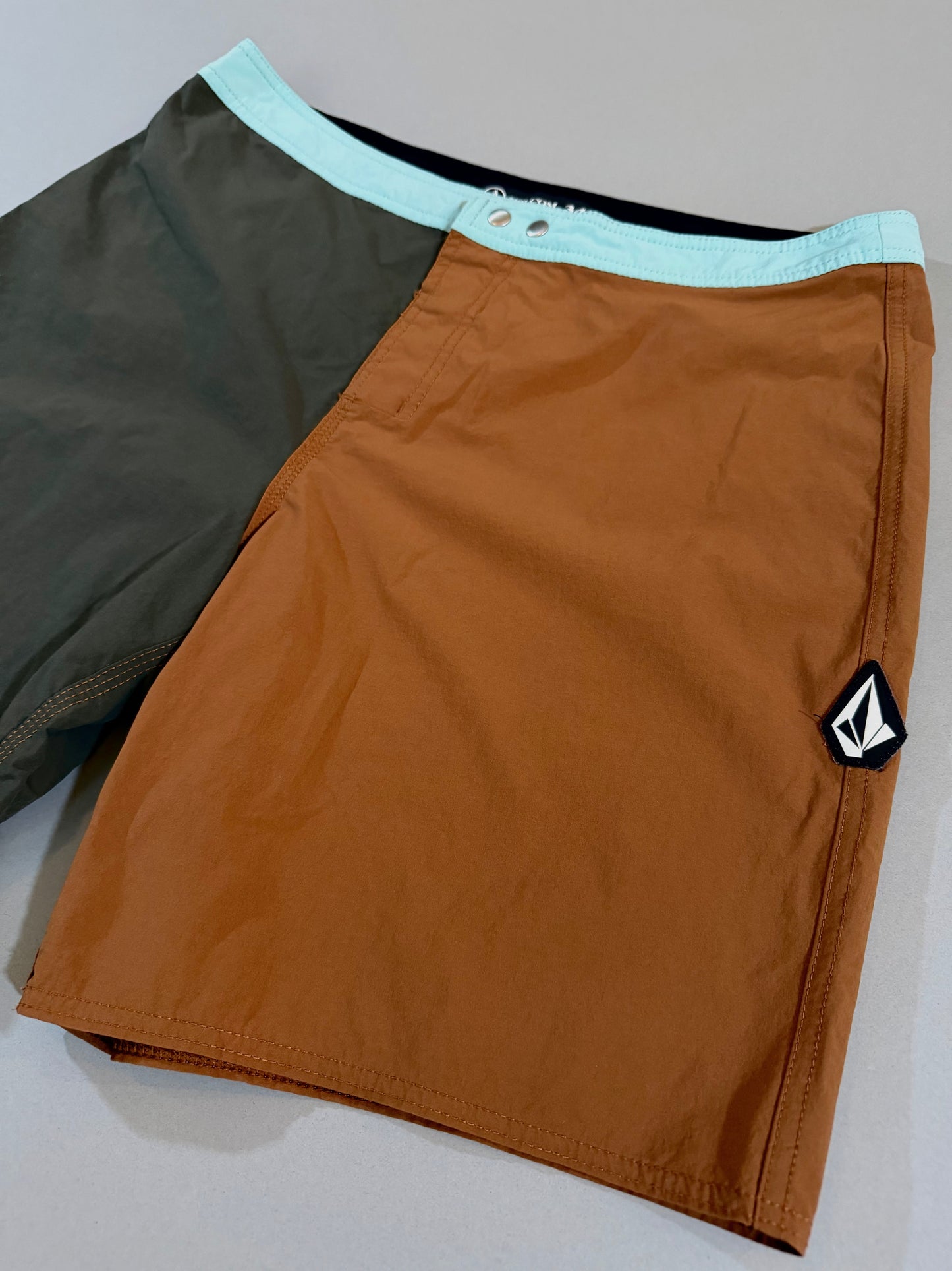 Angled front view highlighting the rust brown panel, aqua waistband, and Volcom Stone logo.