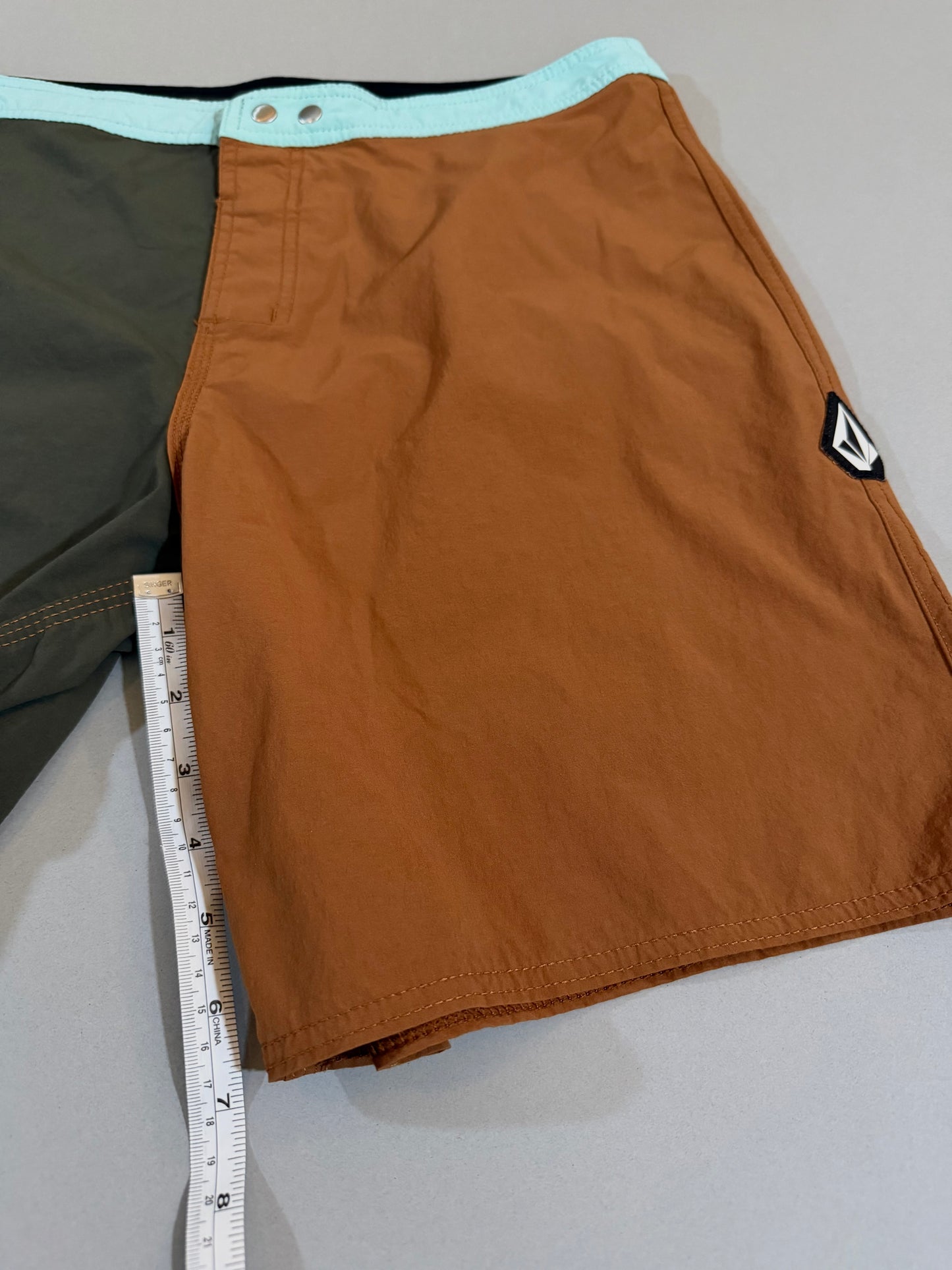 Close-up of the front rust panel and Volcom Stone logo patch on men’s boardshorts, and measuring tape showing 7 inch inseam 