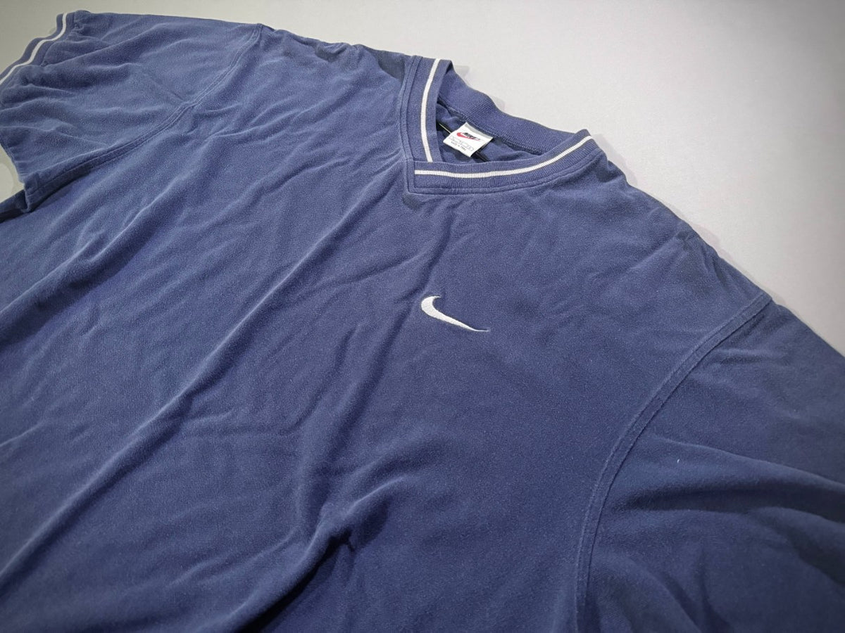 Close angled view of vintage Nike Y2K navy V-neck shirt featuring embroidered white Swoosh and striped collar.
