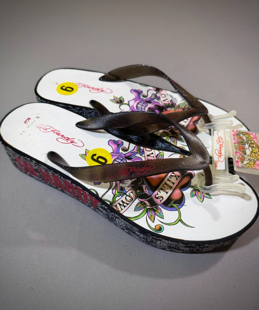 Vintage Ed Hardy women’s platform flip-flops with glitter straps, colorful skull-and-rose footbeds, and black tattoo-print wedge soles, size 9.