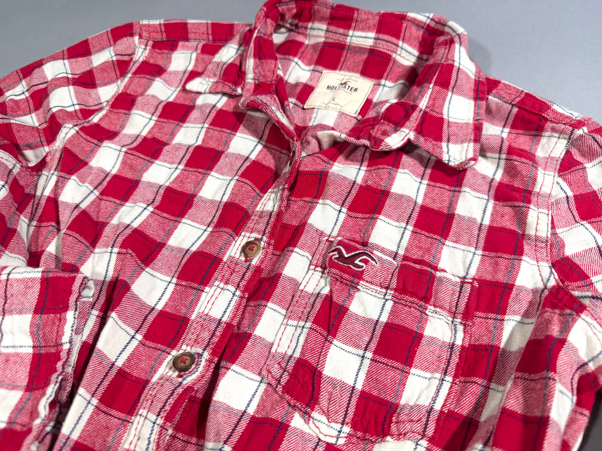 Angled photo of 2000s Hollister plaid flannel shirt showing breast pocket embroidered with maroon seagull logo. 