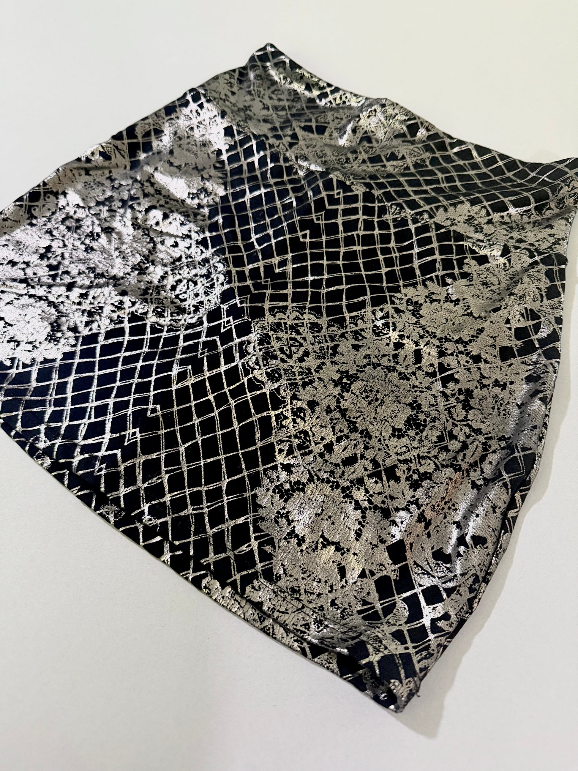 Angled front view of Bebe metallic silver foil stretch mini skirt with reflective lace print.