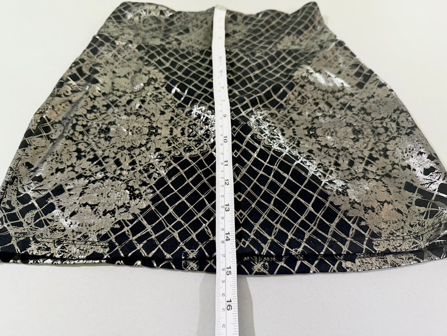 Length measurement of Bebe metallic foil mini skirt showing approximate dimensions.