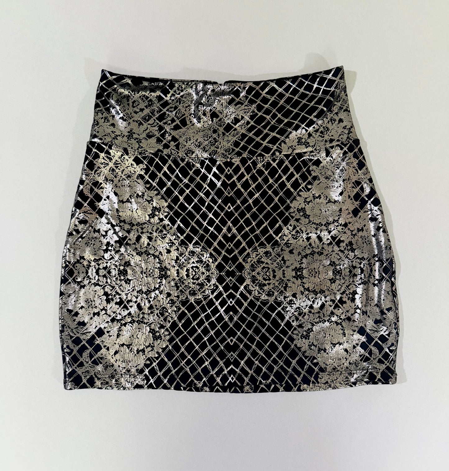 Bebe metallic silver foil mini skirt in black with lace-inspired geometric pattern, front view.