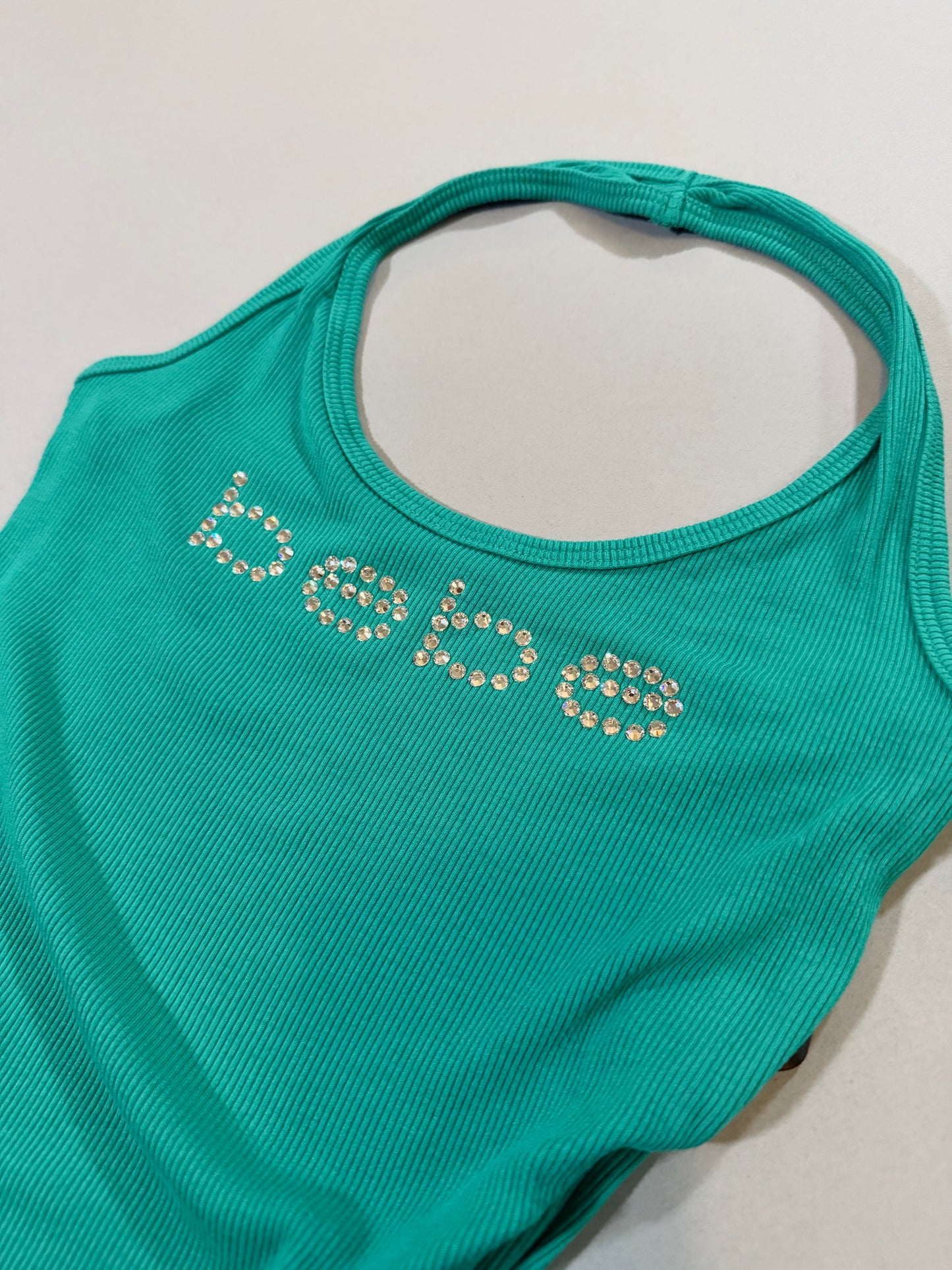 Close-up of the rhinestone Bebe logo on the turquoise ribbed halter dress.
