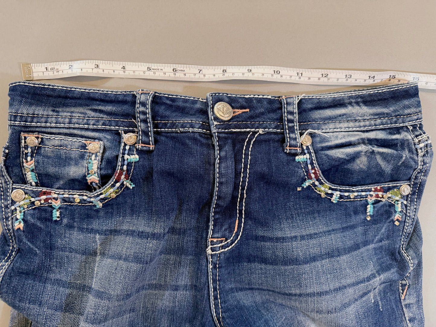 Close up of y2k grace In LA boho denim jeans and measuring tape showing 16 inches (doubled is 32 inches waist)