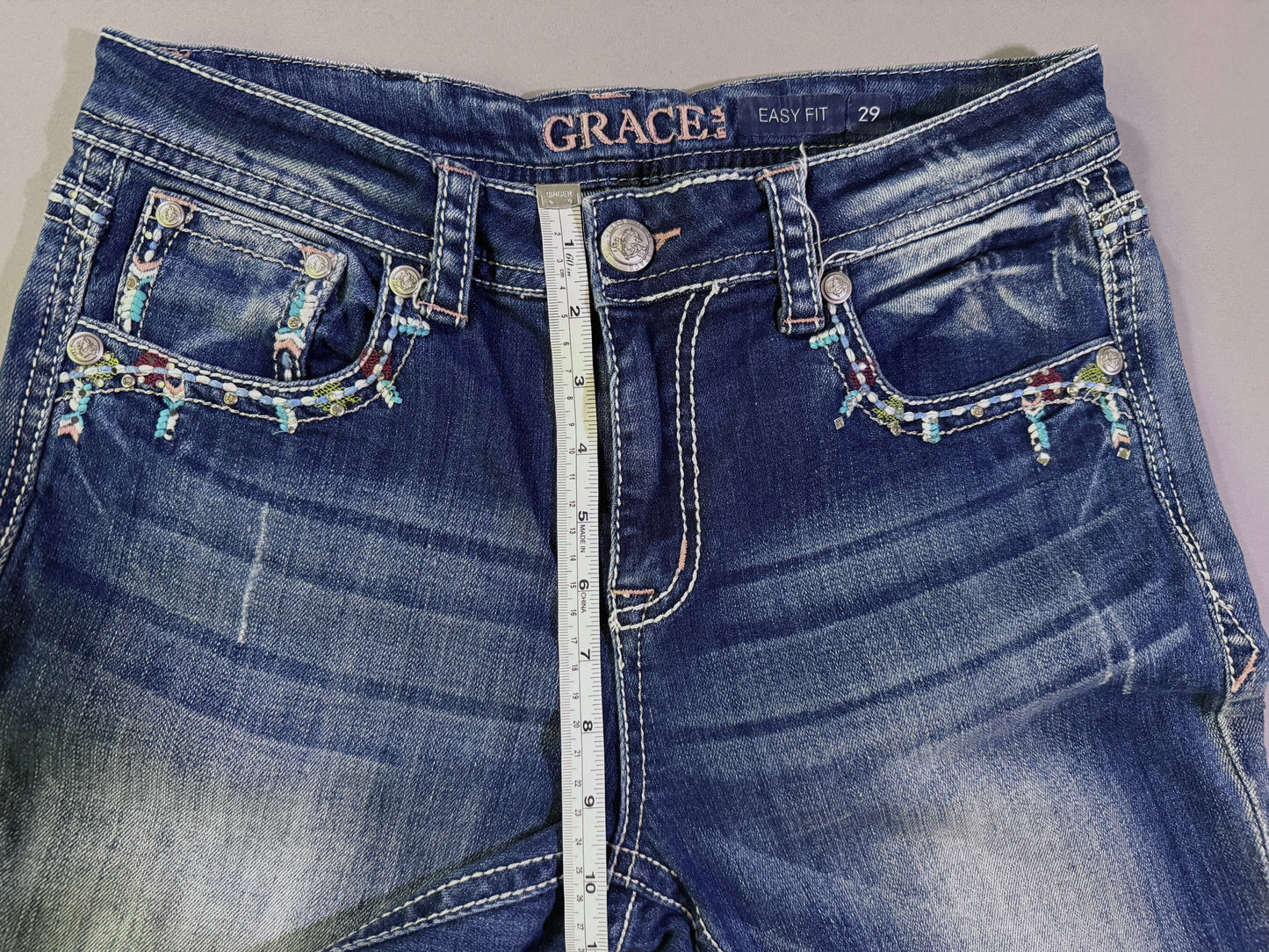 Close up photo of waist of Grace in LA boho bedazzled high rise jeans, with measuring tape showing 10 inch rise. 