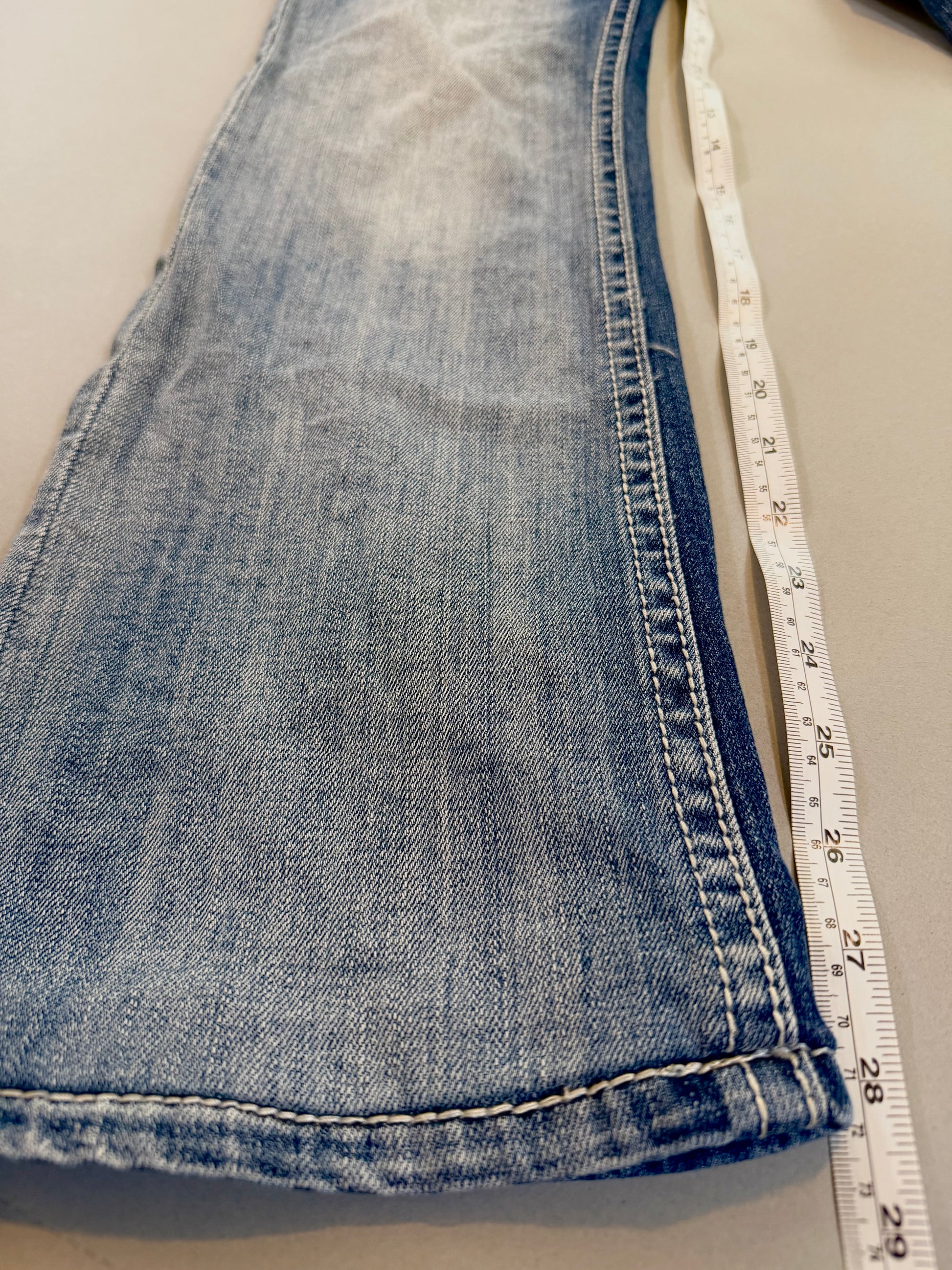 Close up of bootcut flare denim jeans and measuring tape showing 28 inch inseam 