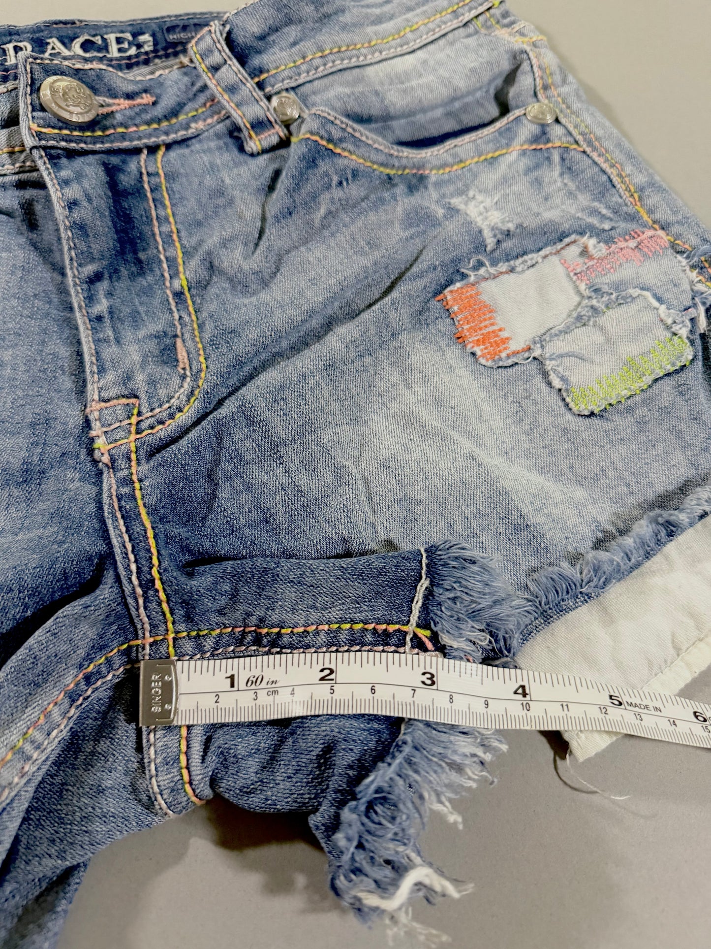 Close-up of the front leg showing distressed denim, pastel patchwork details, faded whiskering, and raw frayed hem.