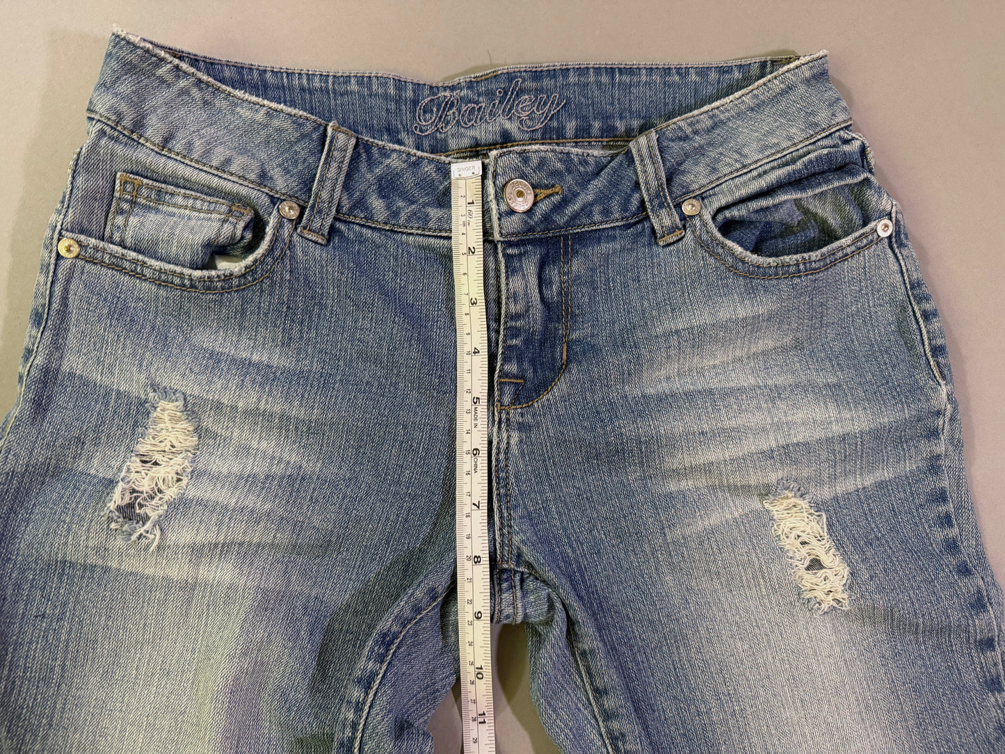 Close up of waist of Delia’s bootcut blue jeans showing Bailey style name, distressing detail, and button/zip fly
