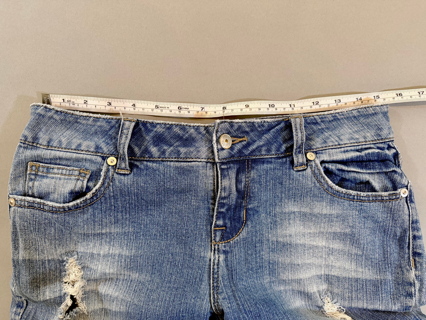 Delia’s Y2K bootcut blue jeans with measuring tape showing 15.5 inches (doubled makes 31 inch waist)