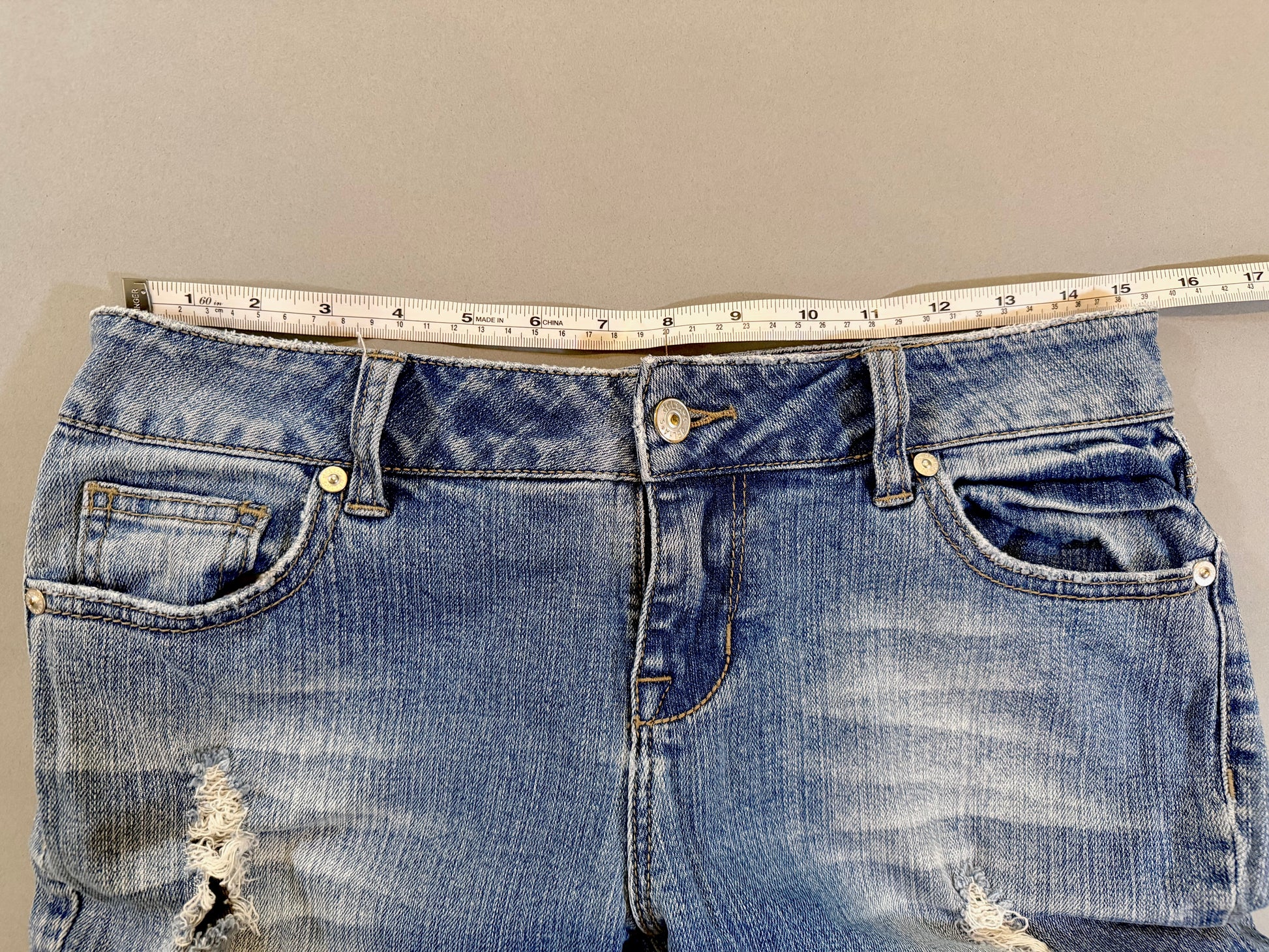 Delia’s Y2K bootcut blue jeans with measuring tape showing 15.5 inches (doubled makes 31 inch waist)