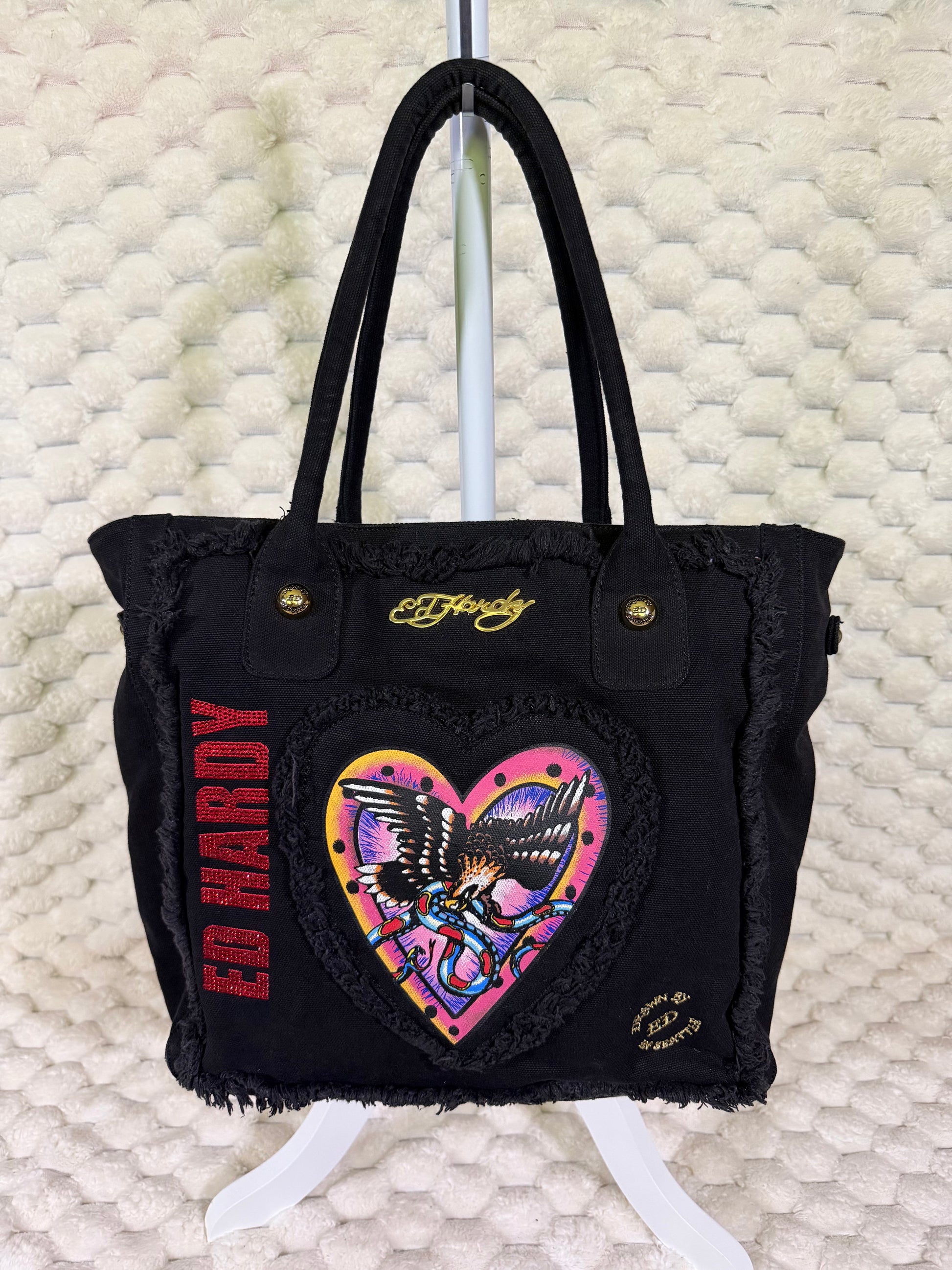 Front view of Y2K Ed Hardy Christian Audigier black canvas tote bag with eagle heart graphic, rhinestone logo and gold hardware.