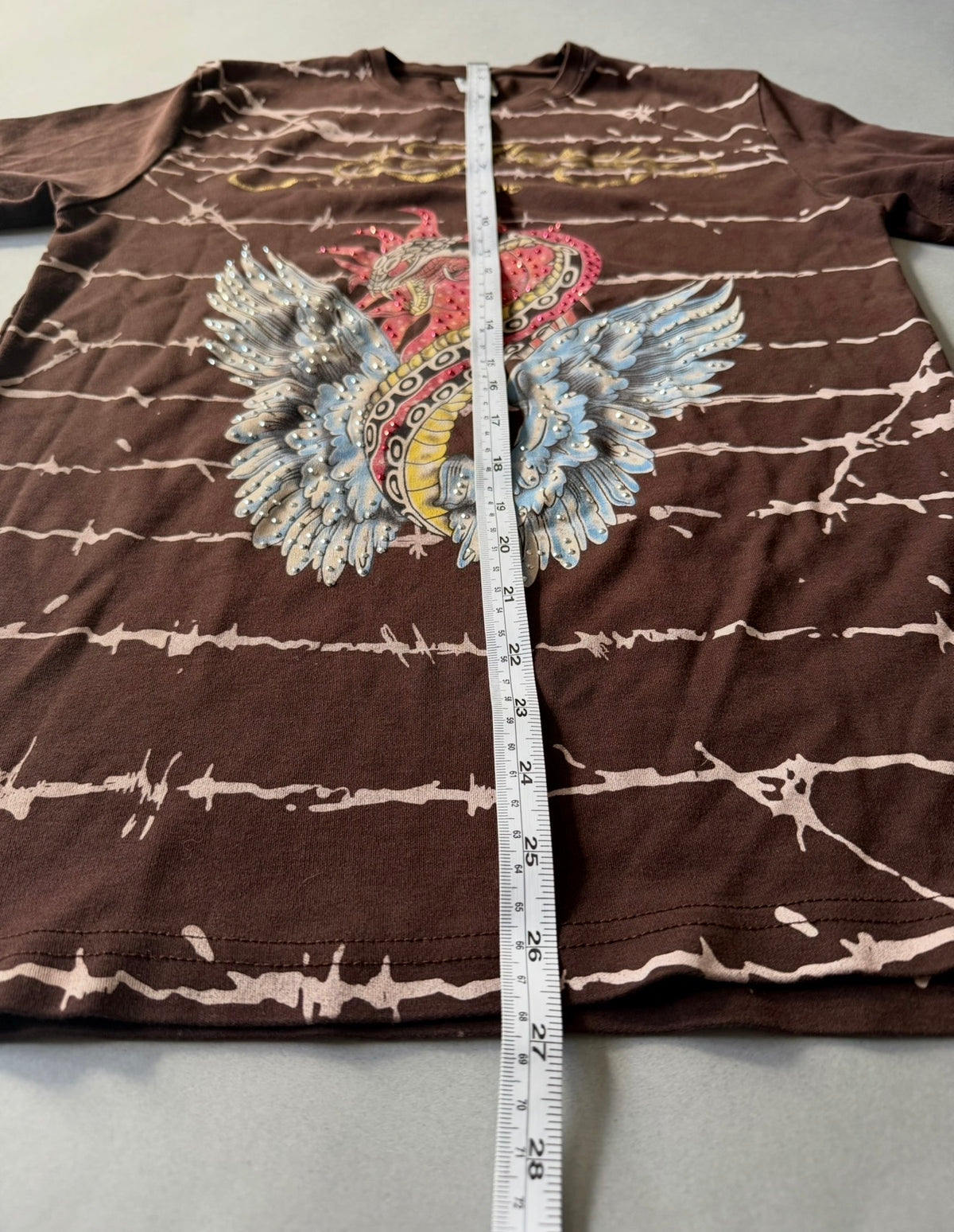 Photo of Ed Hardy t-shirt with measuring tape showing 27 inches length. 