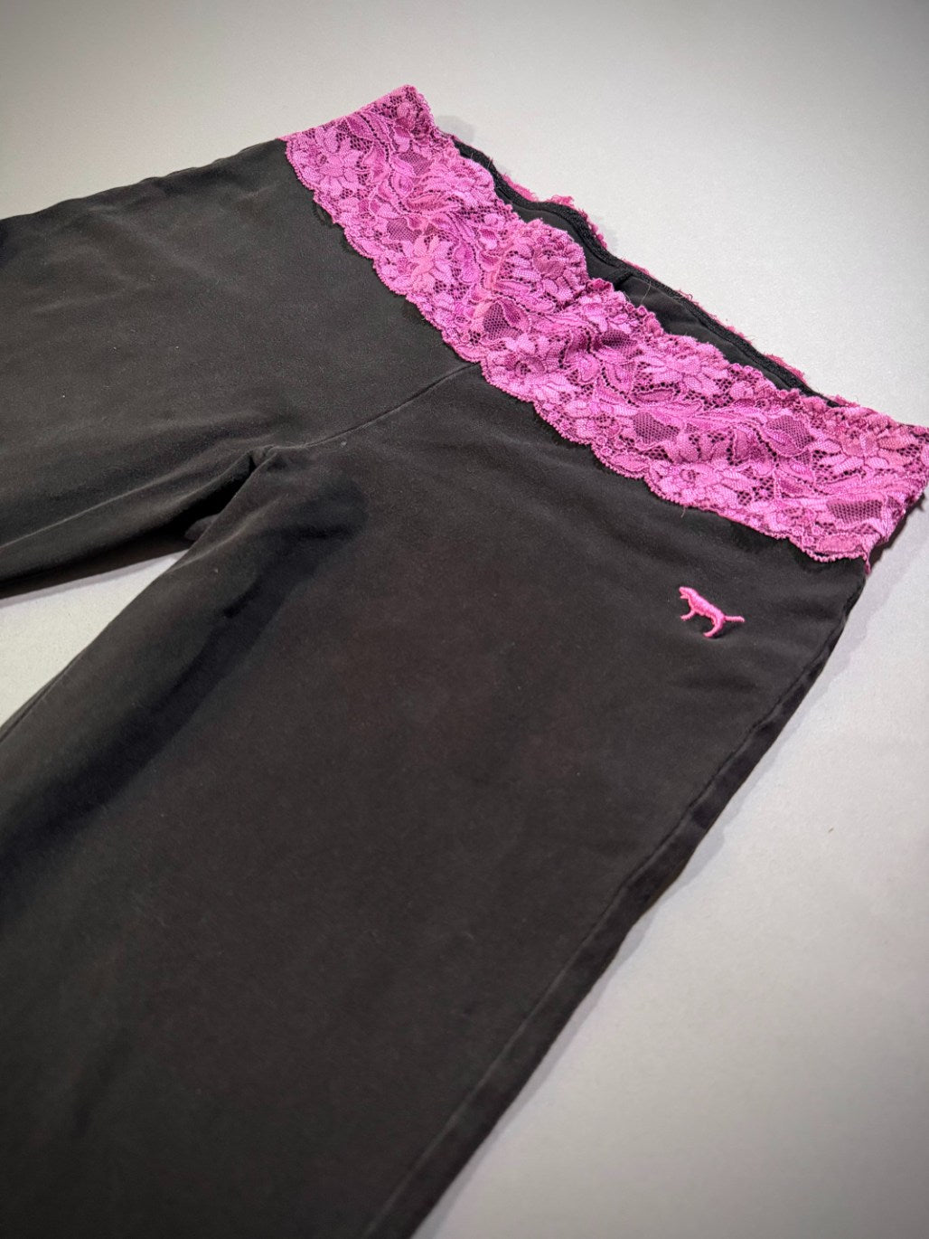 Angled photo of VS PINK yoga pants waist area showing pink lace band and pink dog embroidered logo. 