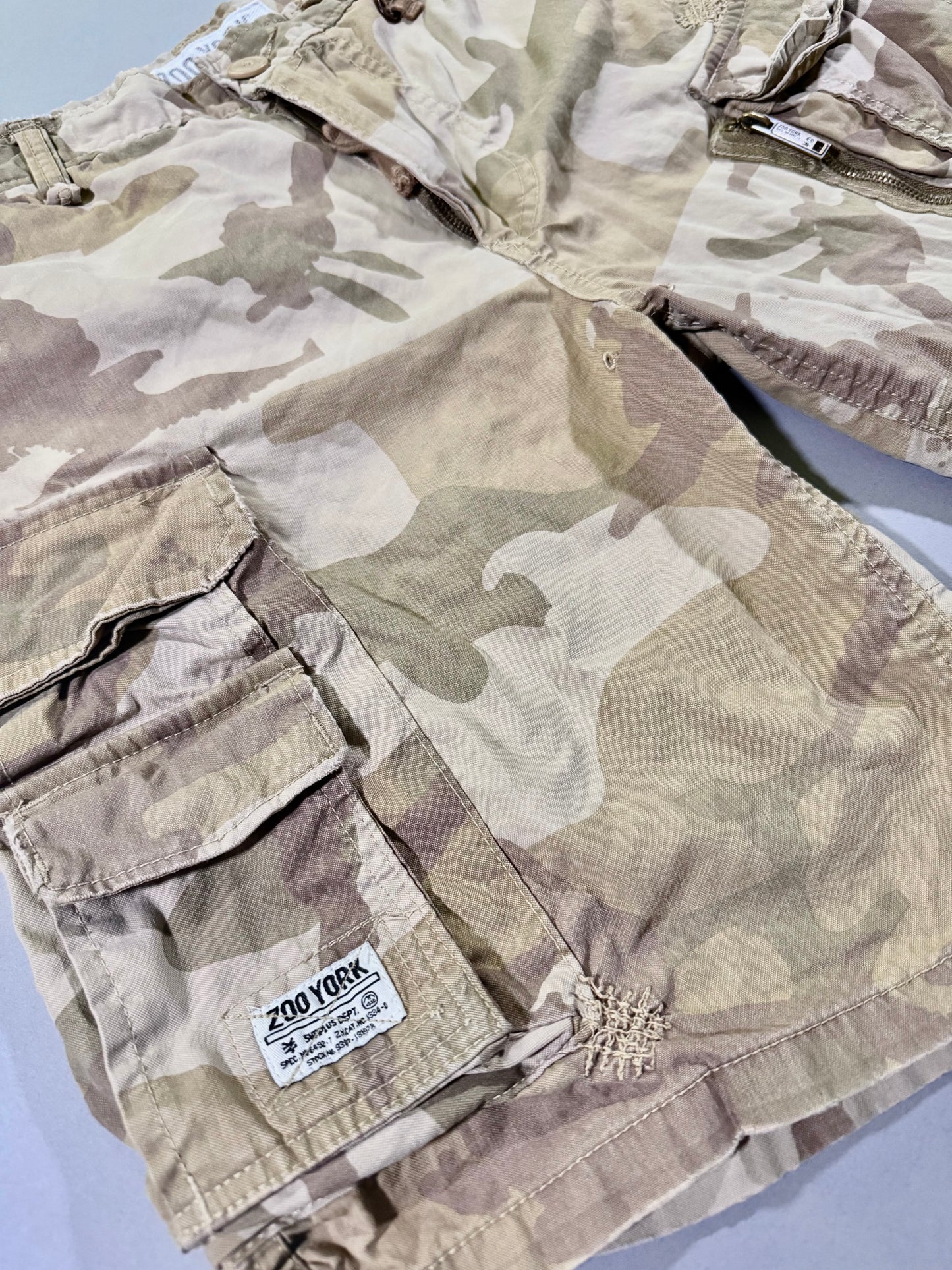 Angled Photo of military surplus-inspired zoo York cargo shorts in desert camo, close-up on faux military specs tag 