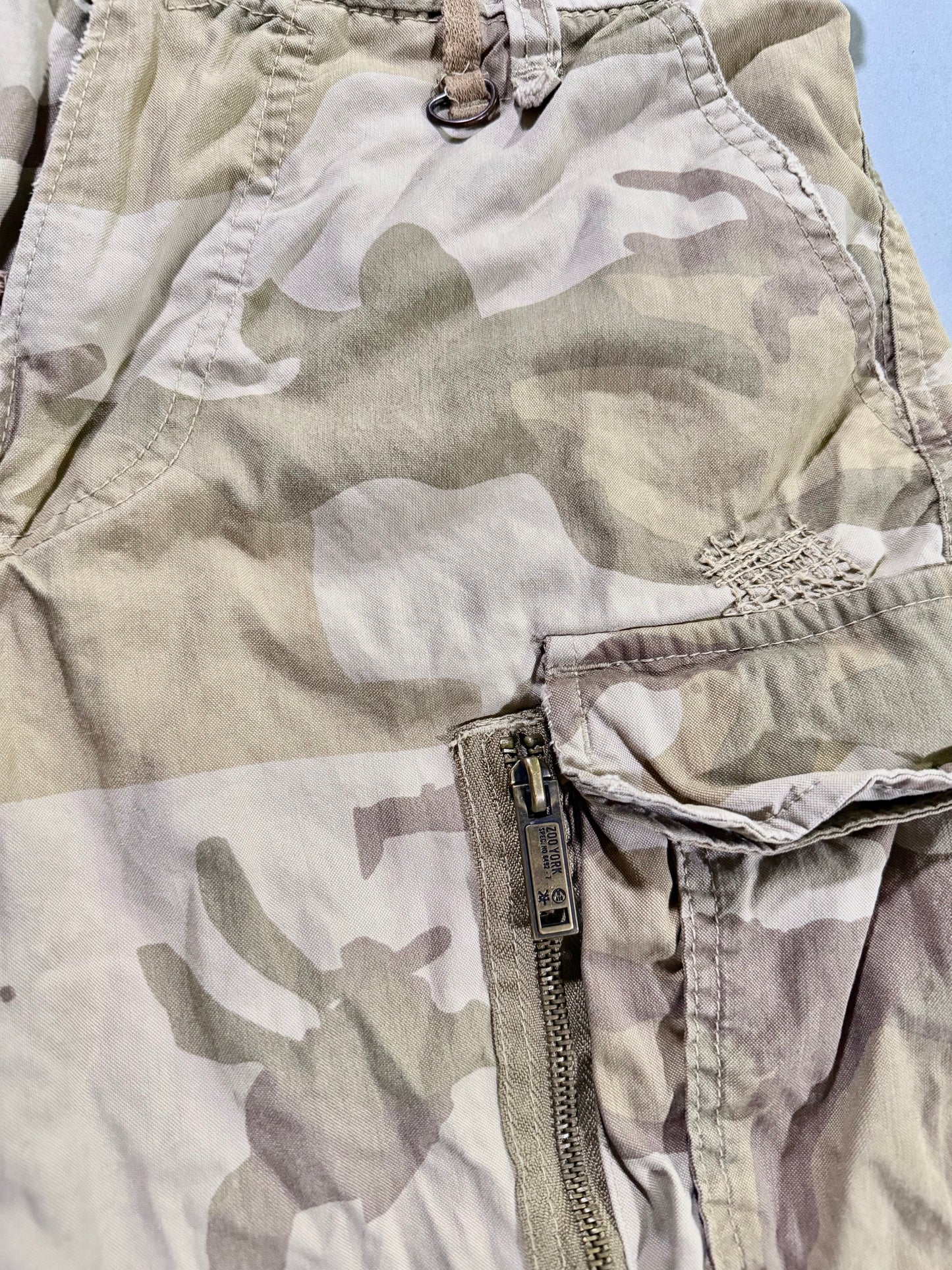 Close-up Photo of military surplus-inspired zoo York cargo shorts in desert camo showing the branded zipper hardware 
