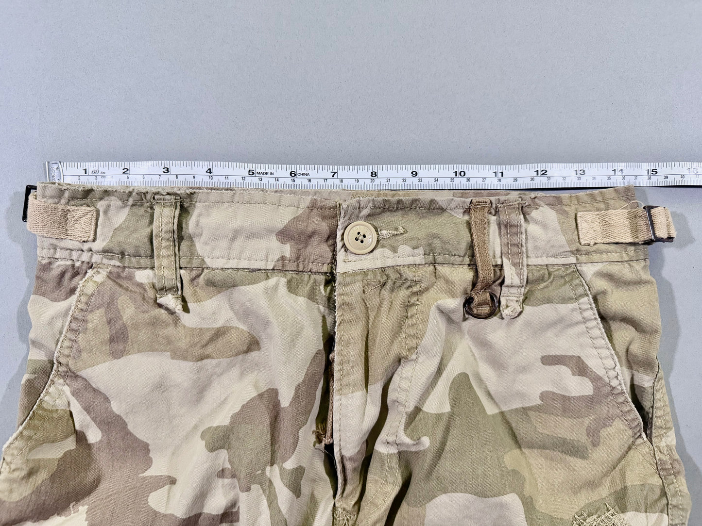 Photo of men’s camo cargo shorts with measuring tape showing 28 inch waist. 