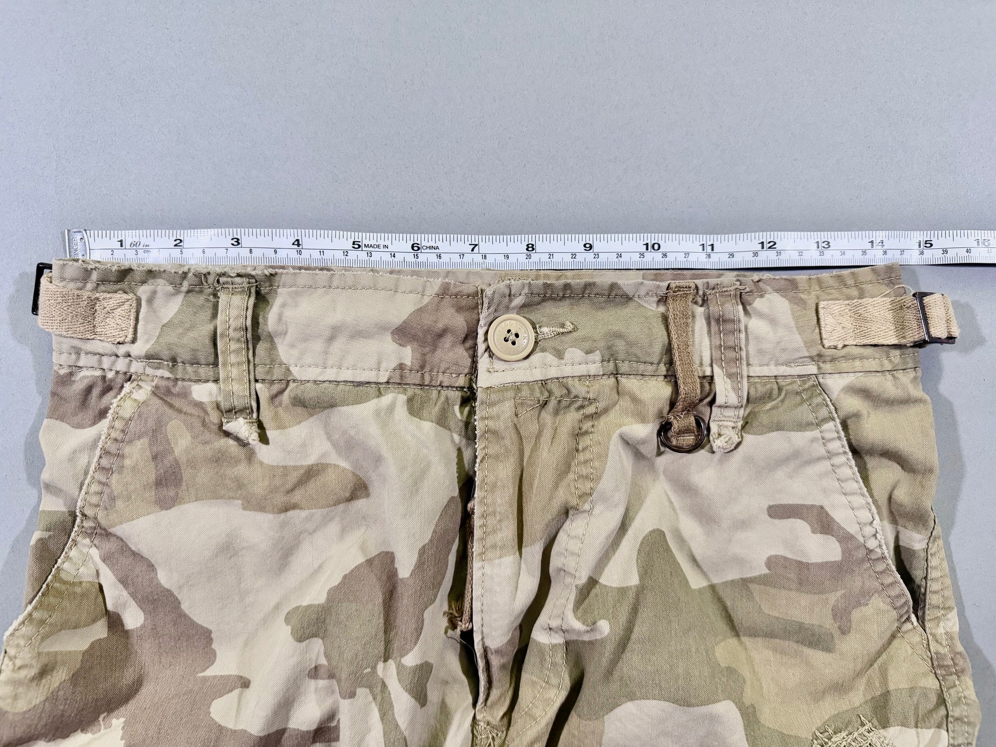 Photo of men’s camo cargo shorts with measuring tape showing 28 inch waist. 